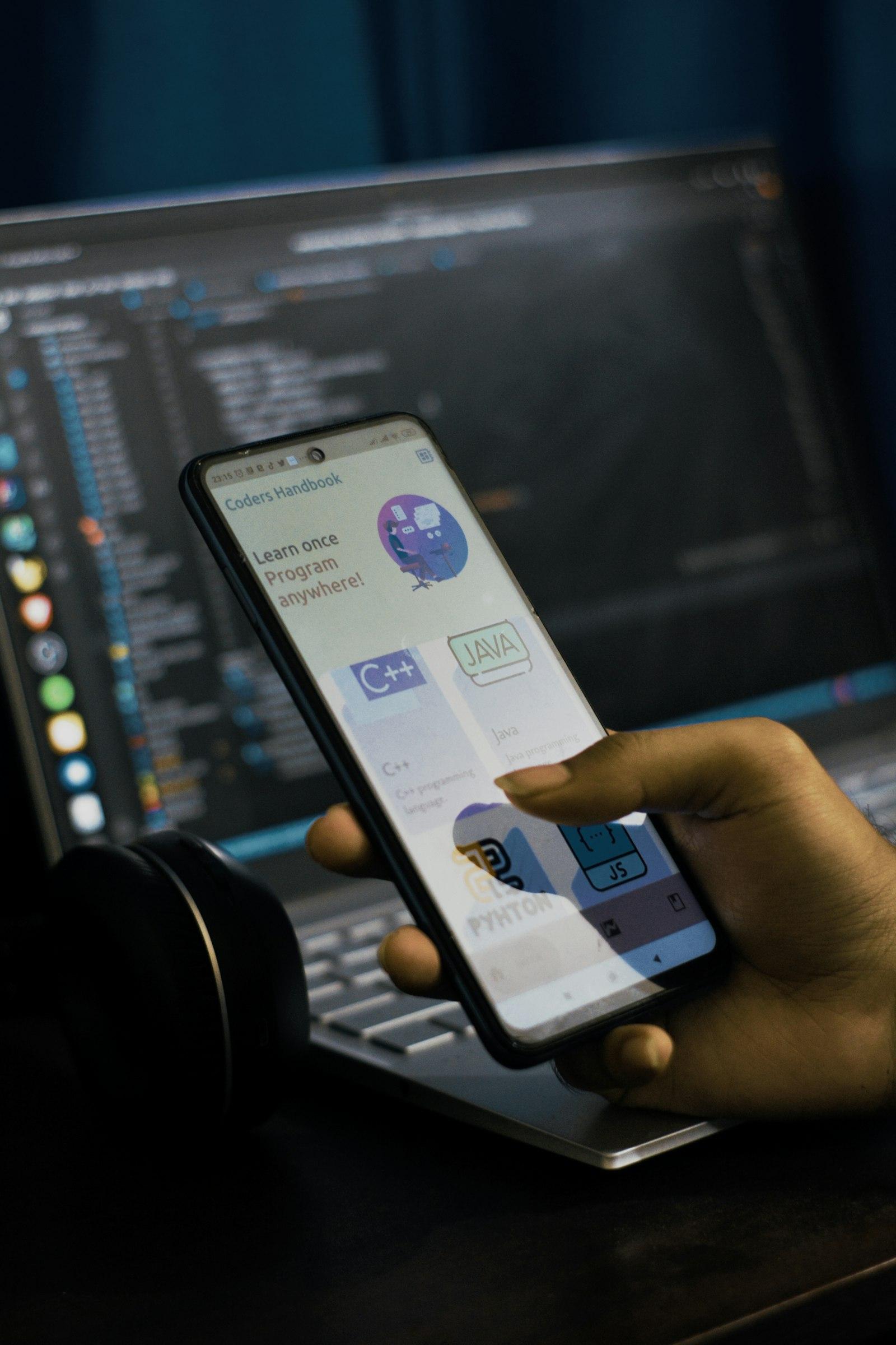 A person holding a phone in front of a laptop